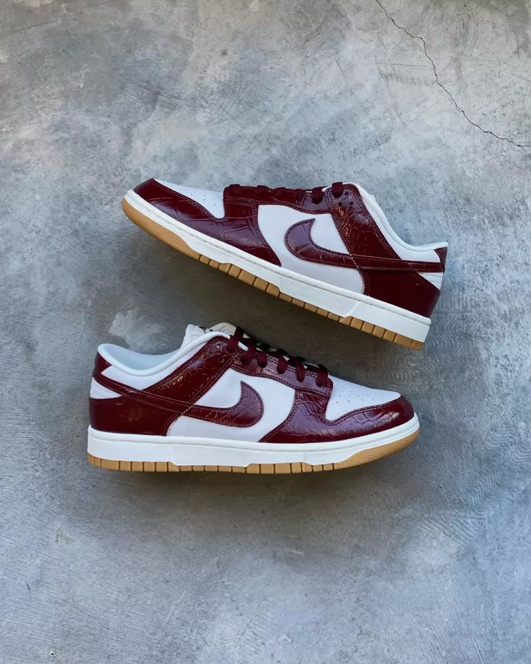 Pair of Dunk Low LX Dark Team Red sneakers with white and dark red panels, textured detailing, and gum soles, displayed on a concrete surface, exclusive in whole Europe. The real deal.