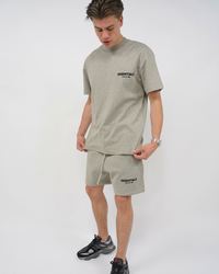 A young man wearing a Fear of God Essentials Dark Oatmeal Summer set with a comfortable short-sleeve top and matching shorts paired with casual black sneakers, showcasing a relaxed summer outfit.