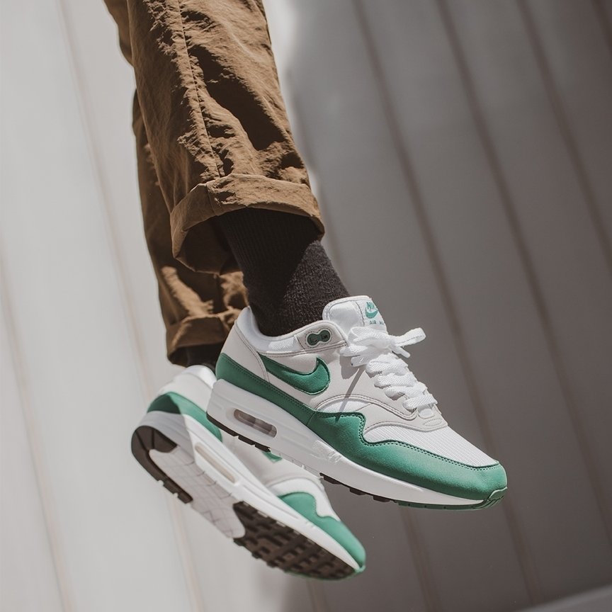 Person wearing Nike Air Max 1 Anniversary Green (2020) sneakers with white and green accents paired with brown pants against a neutral background, showcasing exclusive European sneaker style.