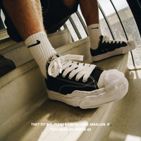 Close-up of person wearing Maison Mihara Yasuhiro Hank OG Sole Canvas Low Black sneakers paired with white Nike socks, showcasing exclusive Europe sneaker style with thick white laces and distinctive sole design. The real deal.