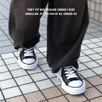 Close-up of feet wearing Maison Mihara Yasuhiro Peterson 23 OG Sole Canvas Low Black sneakers on tiled floor, styled with loose black pants, showcasing exclusive European sneaker fashion. The real deal.