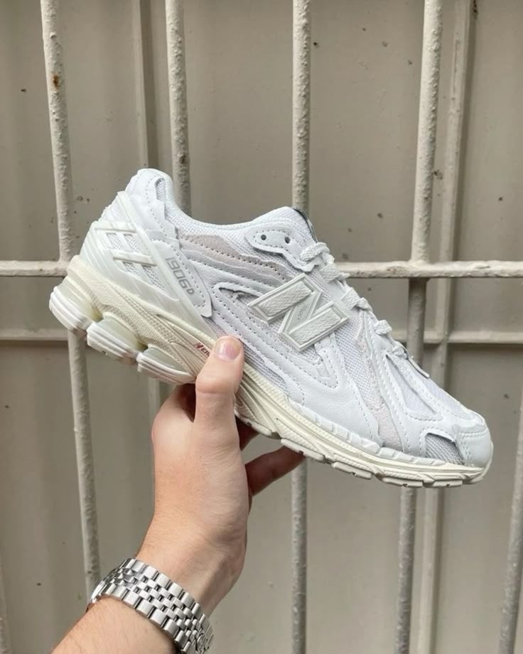 Hand holding a white sneaker with leather and mesh detailing, showcasing the New Balance 1906D Protection Pack White Leather sneaker, known as the real deal exclusive in Europe.