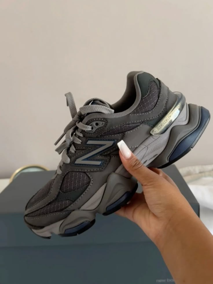 Hand holding a New Balance 9060 Castlerock Grey Navy sneaker showcasing its modern design and mixed grey and navy tones, representing exclusive sneakers in Europe, the real deal.