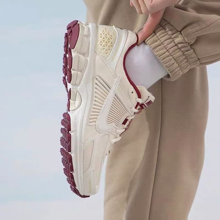A person wearing beige pants holds a white and burgundy sneaker with detailed sole grip, showcasing the Nike Zoom Vomero 5 Valentine's Day (2024), exclusive sneakers in Europe, the real deal.
