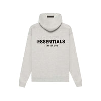Back view of a light oatmeal hoodie with bold black "ESSENTIALS FEAR OF GOD" text, part of the Fear of God Essentials Light Oatmeal Full set, showcasing casual streetwear style.