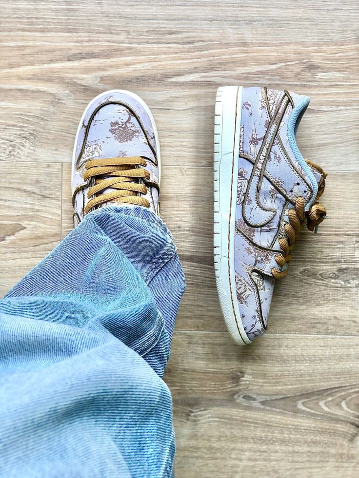 Pair of SB Dunk Low Premium Pastoral Print sneakers featuring a soft blue floral pattern with brown laces, styled casually with light blue denim on a wooden floor, the real deal.