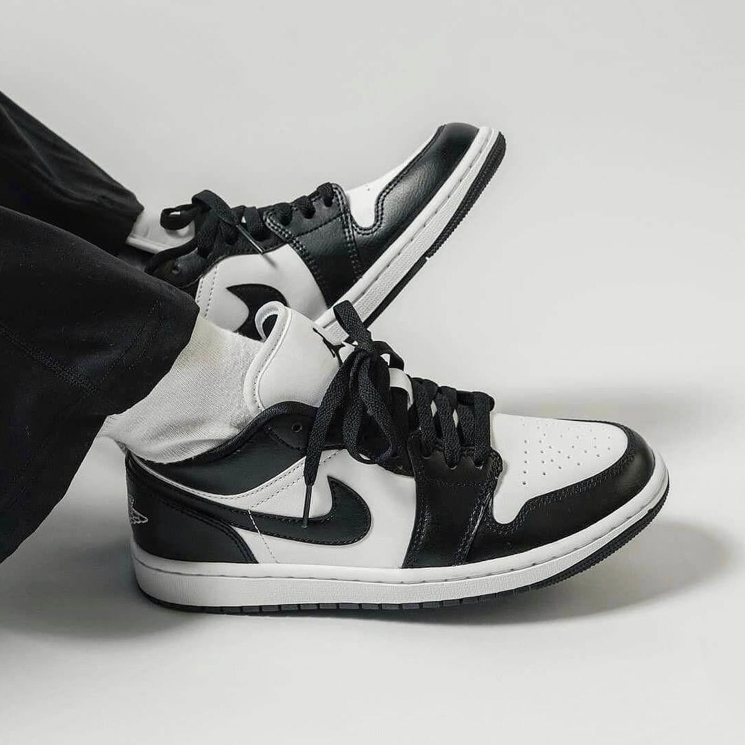 Person wearing Nike Air Jordan 1 Low Panda sneakers in black and white, styled with black pants and white socks, showcasing exclusive sneaker design in Europe. The real deal.