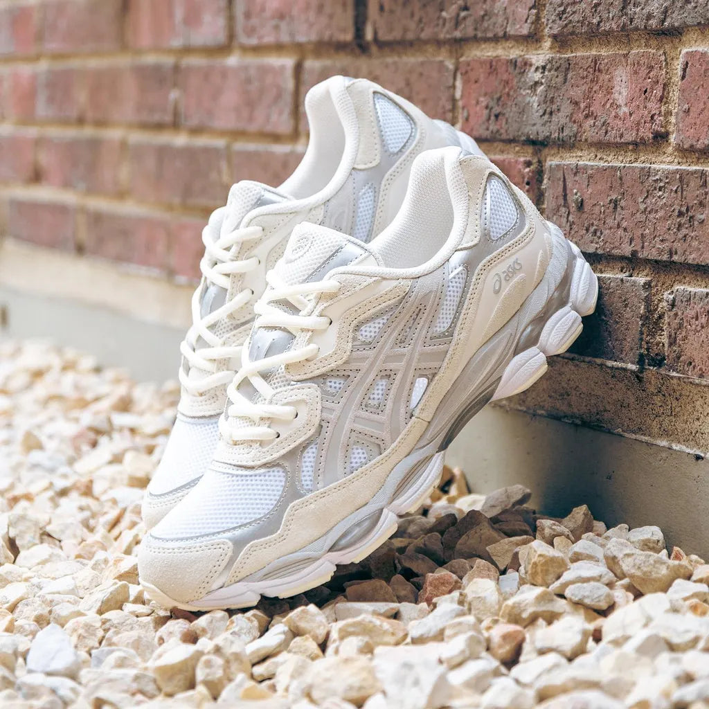 ASICS Gel-NYC White Oyster Grey sneakers resting on stones against a brick wall, showcasing breathable mesh and supportive overlays with a stylish, exclusive design for sneaker enthusiasts in Europe. The real deal.