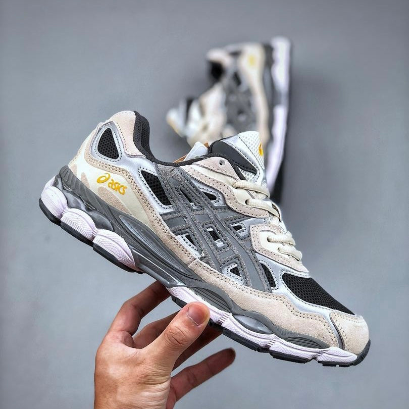 A hand holding an ASICS Gel-NYC Black Clay Grey sneaker featuring a mix of black, grey, and beige tones with the ASICS logo in yellow, highlighting exclusive European sneaker style.