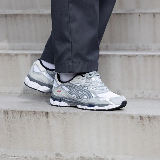 Person wearing ASICS Gel-NYC White Steel Grey sneakers standing on concrete stairs, showcasing stylish trainers exclusive to Europe with a modern urban look.