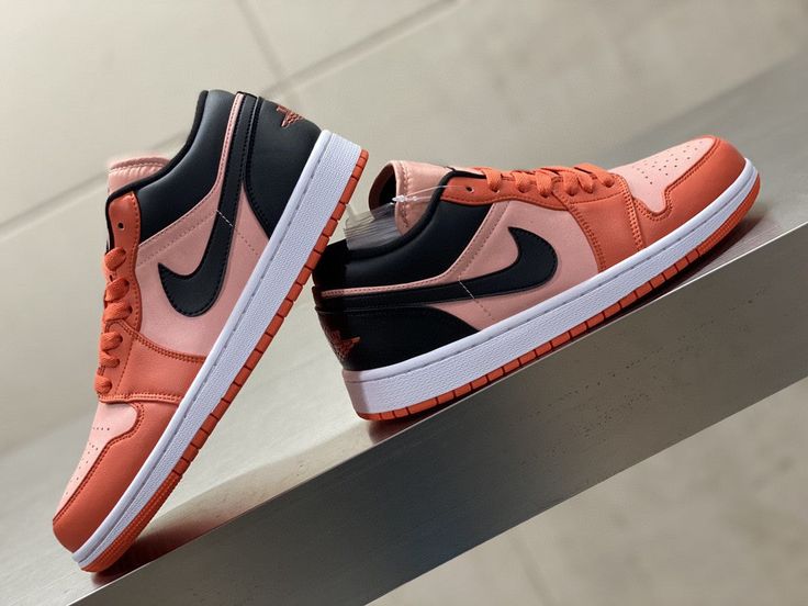 Pair of exclusive Air Jordan 1 Low Orange Black sneakers with vibrant orange and black leather, displayed on a modern metallic surface, representing the real deal in European sneaker style.