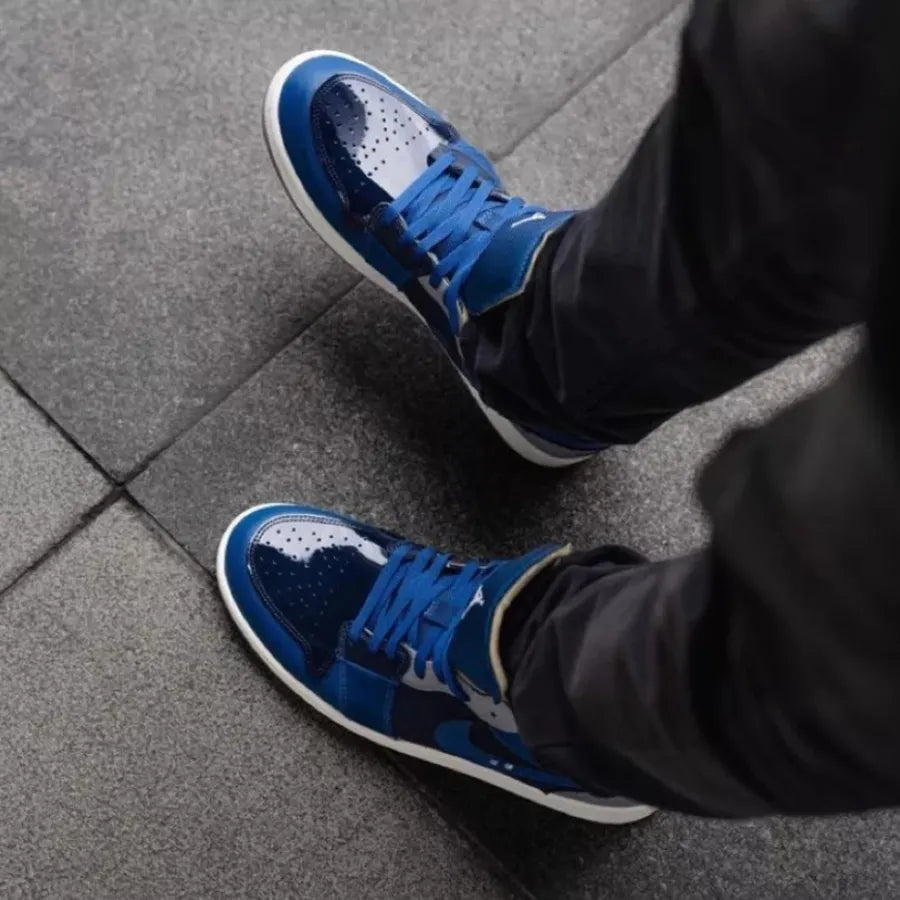 Person wearing blue and navy sneakers walking on gray tiled floor, showcasing the Air Jordan 1 Low SE Craft Obsidian in an urban setting.