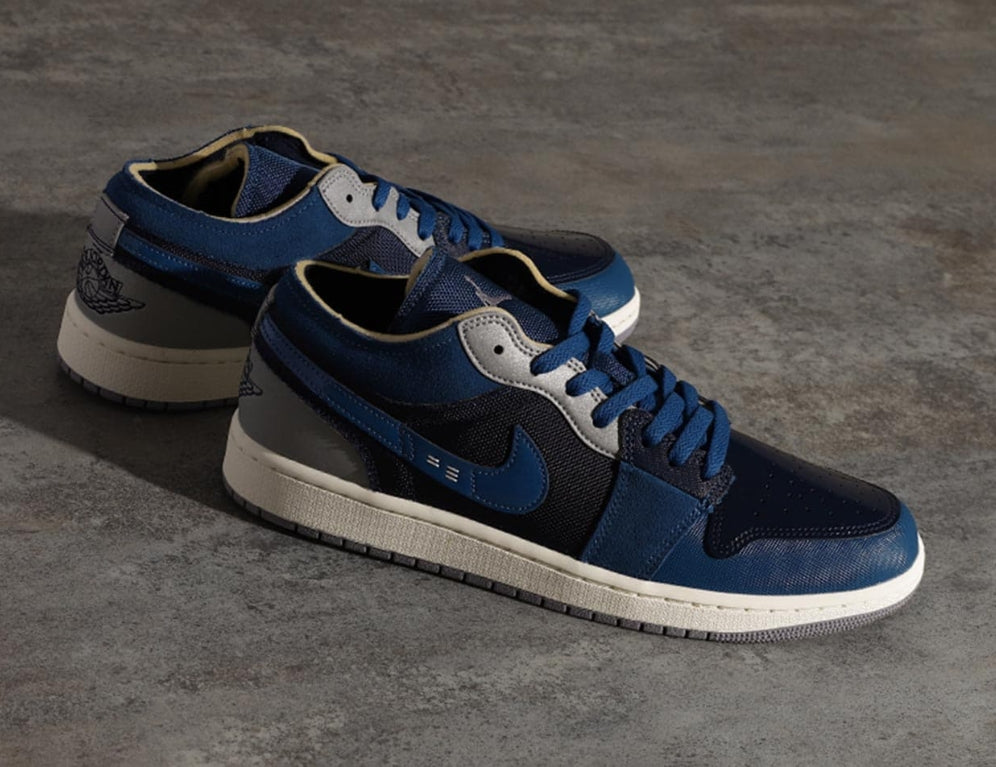 Pair of Air Jordan 1 Low SE Craft Obsidian sneakers in navy blue and black with white soles, displayed on a textured dark surface, showcasing exclusive European style.