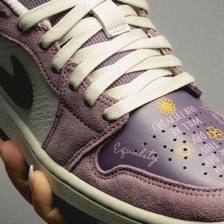 Close-up of a purple and cream Air Jordan 1 Low Unity sneaker featuring detailed text and flower designs on the toe box, emphasizing equality and unity messages.