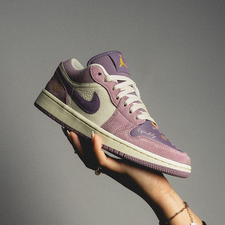 A hand holding a stylish Air Jordan 1 Low Unity sneaker in shades of purple and cream, showcasing exclusive design and premium materials.