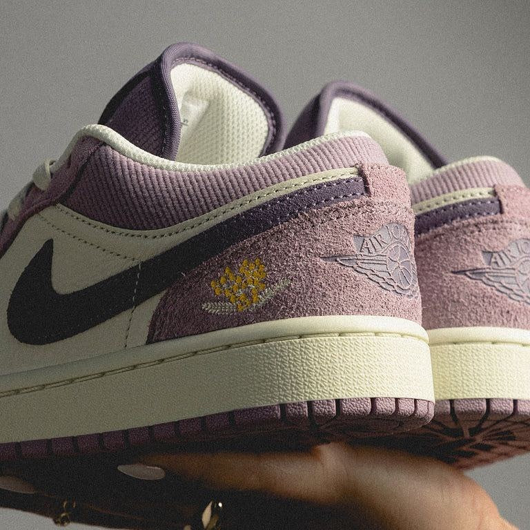 Close-up of purple, cream, and black Air Jordan 1 Low Unity sneakers showcasing suede and fabric textures with the exclusive European design detail and subtle wing logo embossed on the heel, the real deal.