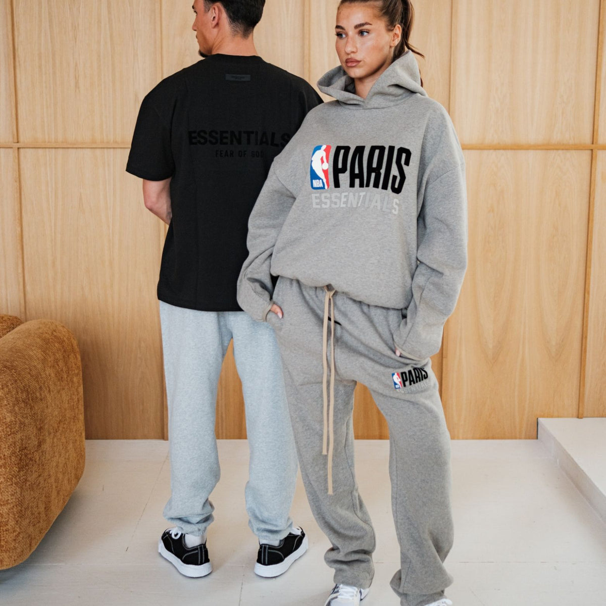 Fear of God Essentials NBA Paris set gedragen door twee personen, grijze hoodie met logo en grijze joggingbroek