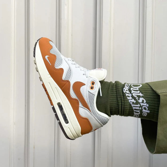 Nike Air Max 1 Patta Waves Monarch sneaker in white and orange with a wavy design, worn with green socks and matching pants, showcasing exclusive European sneaker style.