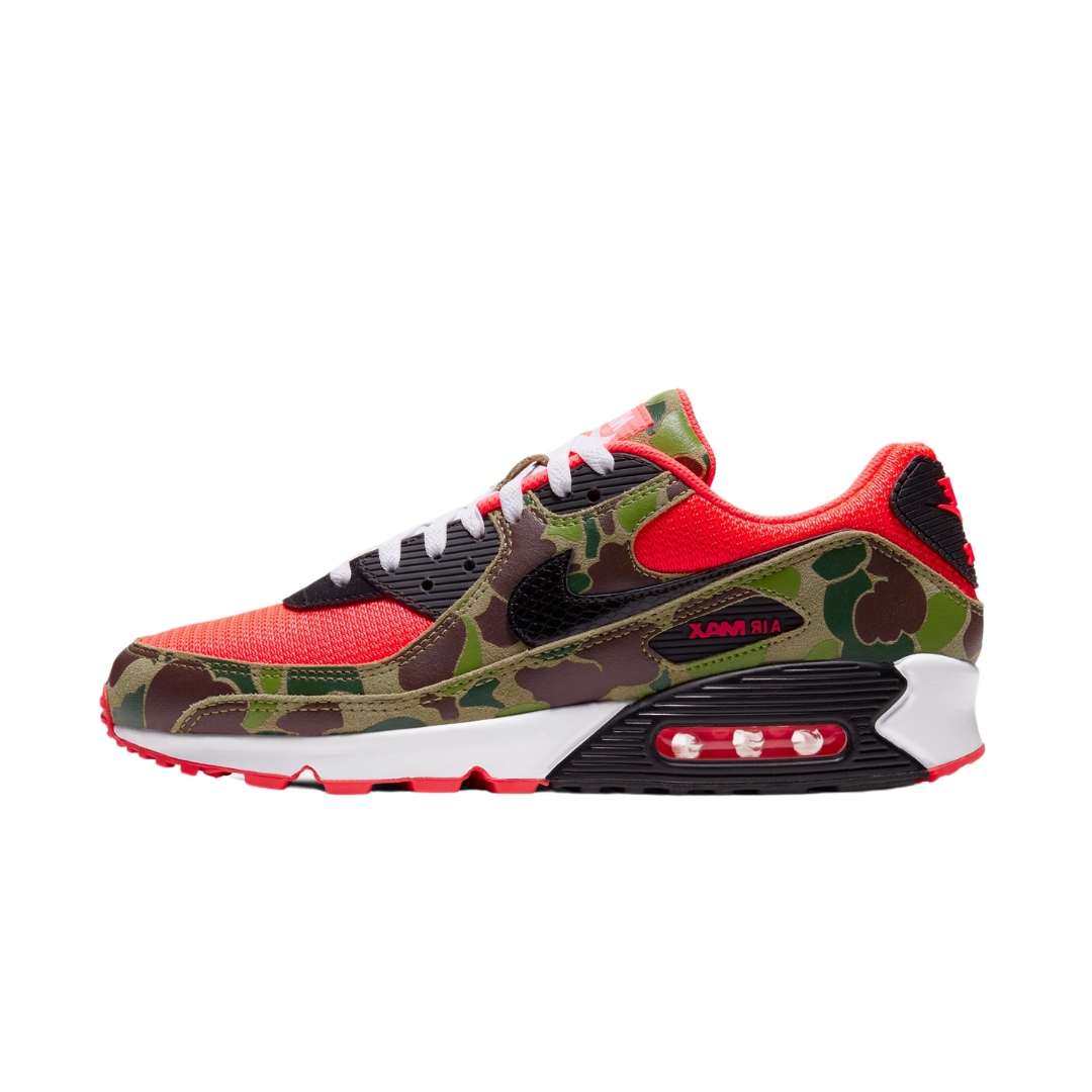 Side view of Nike Air Max 90 Reverse Duck Camo sneaker featuring camouflage pattern with bright red and black accents, white laces, and visible Air Max cushioning, exclusive in Europe.