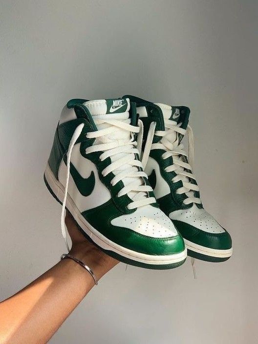 A hand holding a pair of Nike Dunk High Australia sneakers in green and white, showcasing their classic high-top design and clean leather finish.