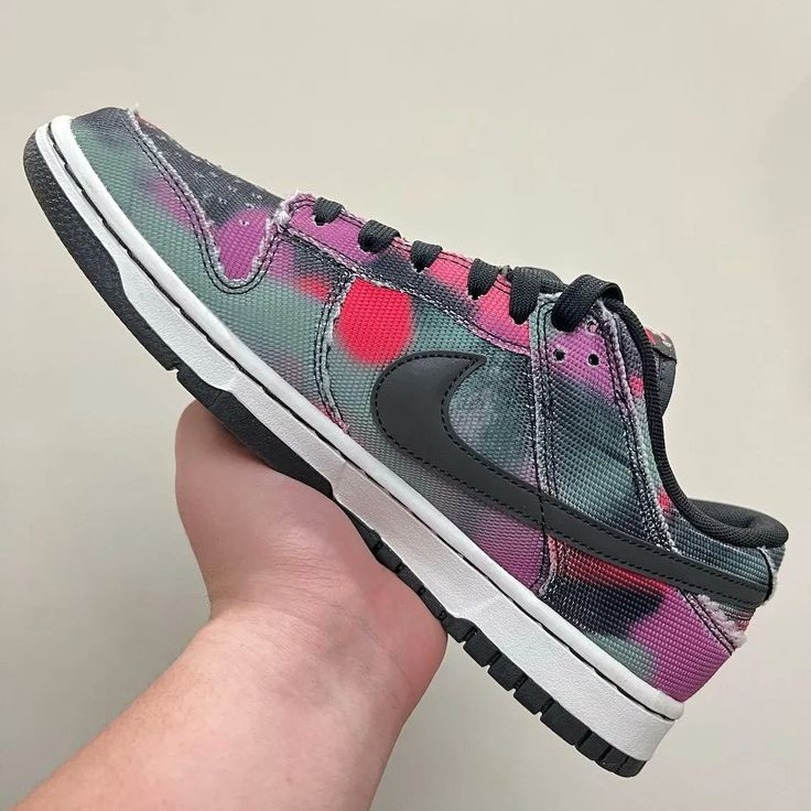Hand holding a Nike Dunk Low Graffiti Pink sneaker featuring a black swoosh, pink and gray graffiti-style accents, black laces, and a white midsole with a black outsole, The real deal.