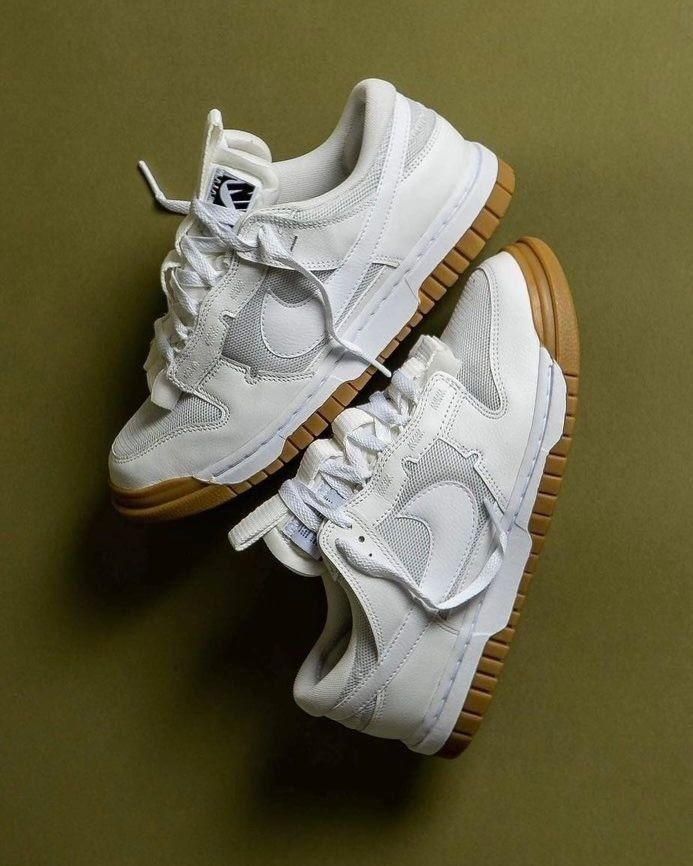 Pair of Nike Dunk Low Remastered White Gum sneakers with white leather upper and gum sole, displayed on an olive background, perfect exclusive sneaker choice across Europe. The real deal.