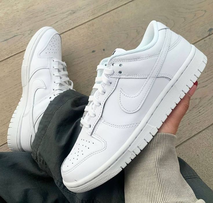 Close-up of Nike Dunk Low Triple White (2021) sneakers featuring clean white leather design, worn with casual pants on a wooden floor, showcasing exclusive sneaker style.