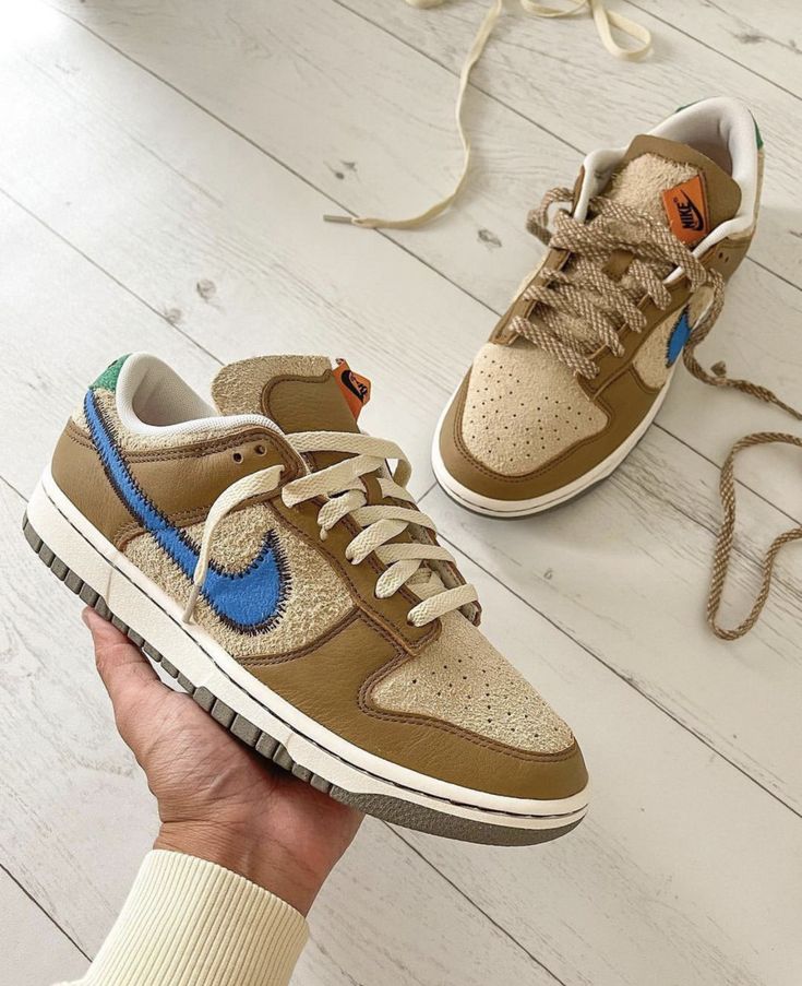 Pair of Nike Dunk Low size? Dark Driftwood sneakers featuring a mix of textured beige and brown leather with a distinctive blue Nike swoosh, displayed on a light wooden floor. The real deal exclusive sneakers in whole Europe.