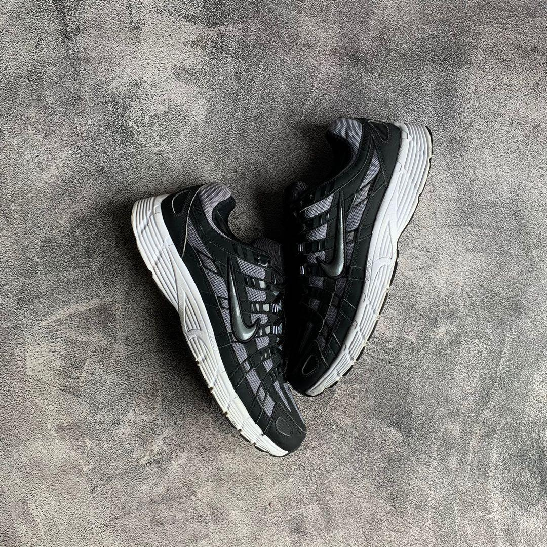 Pair of Nike P-6000 Black Cool Grey sneakers with black and grey mesh and synthetic upper, featuring white cushioned soles, displayed on a textured concrete surface.