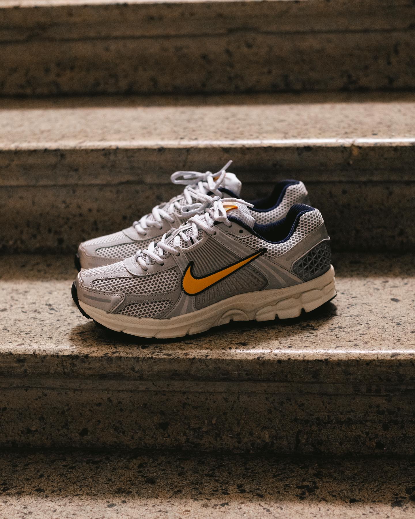Pair of Nike Zoom Vomero 5 Pure Platinum Laser Orange sneakers resting on stone steps, showcasing breathable mesh and bright orange swoosh, perfect exclusive trainers in Europe.