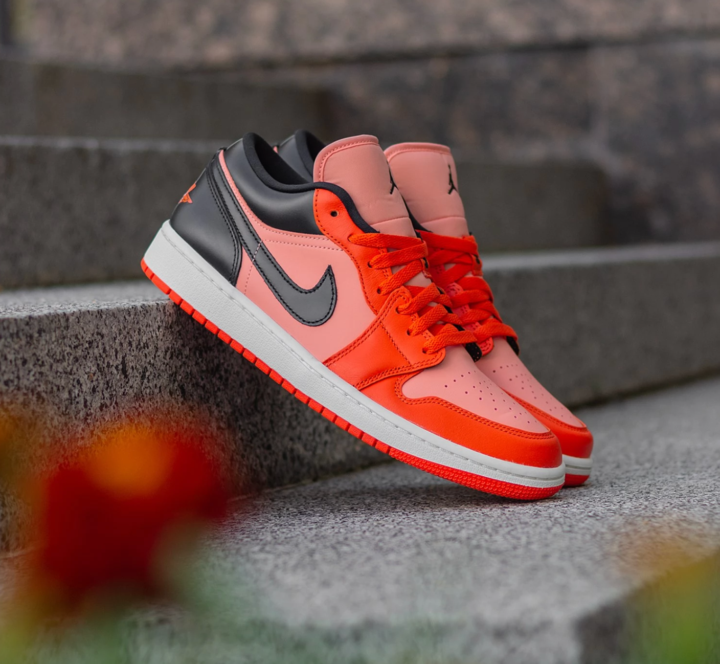 Air Jordan 1 Low Orange Black sneakers displayed on concrete steps, showcasing vibrant orange, black, and pink tones with a sleek design, perfect exclusive trainers for sneaker enthusiasts.