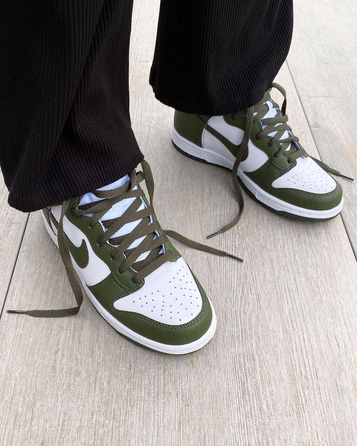 Person wearing Nike Dunk High Cargo Khaki sneakers with olive green and white design, styled with black pants on a light wood floor, showcasing exclusive European sneaker fashion.