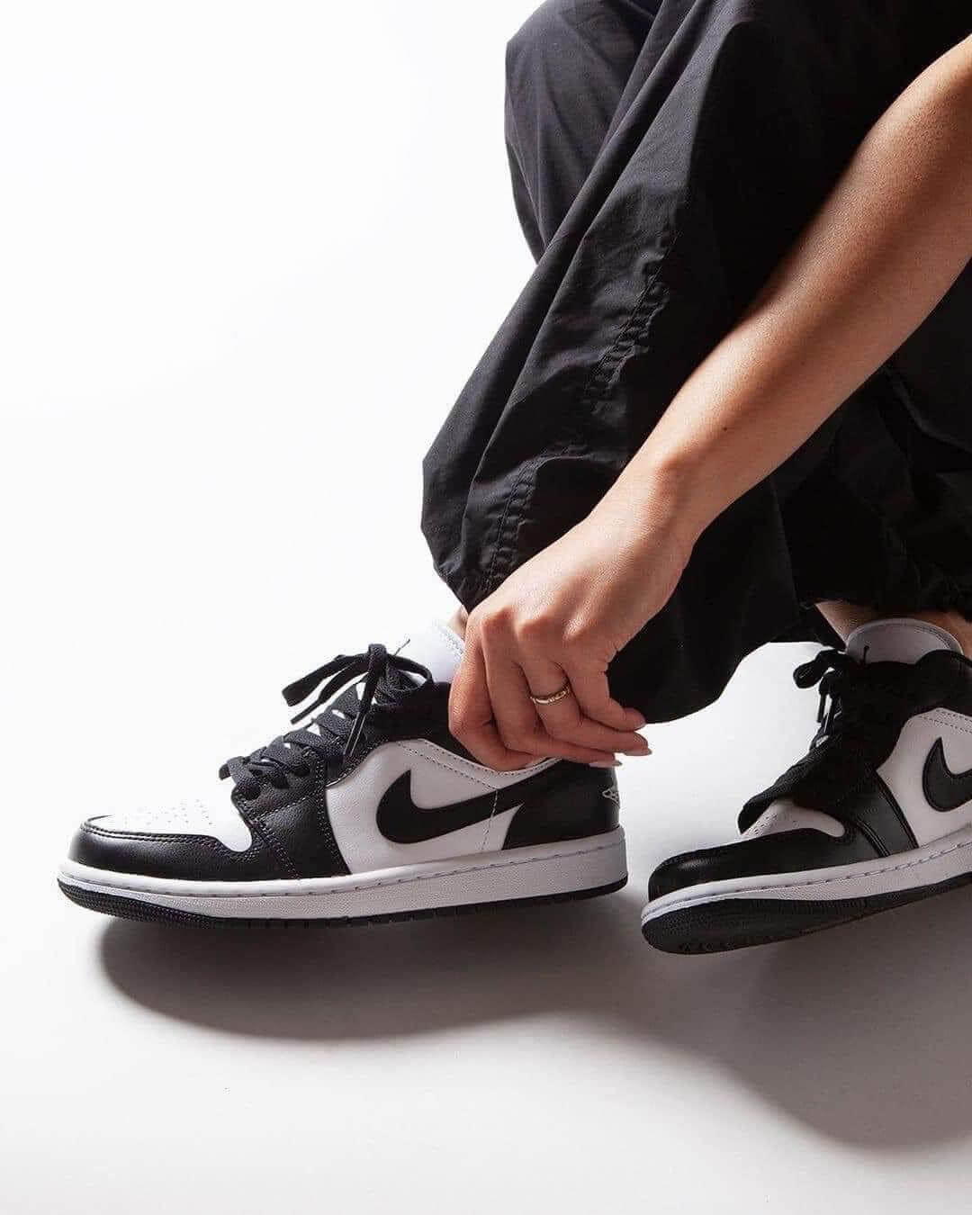 Person wearing black pants lacing up black and white Nike Air Jordan 1 Low Panda sneakers, showcasing exclusive European sneaker style from SneakerAsk, The real deal.