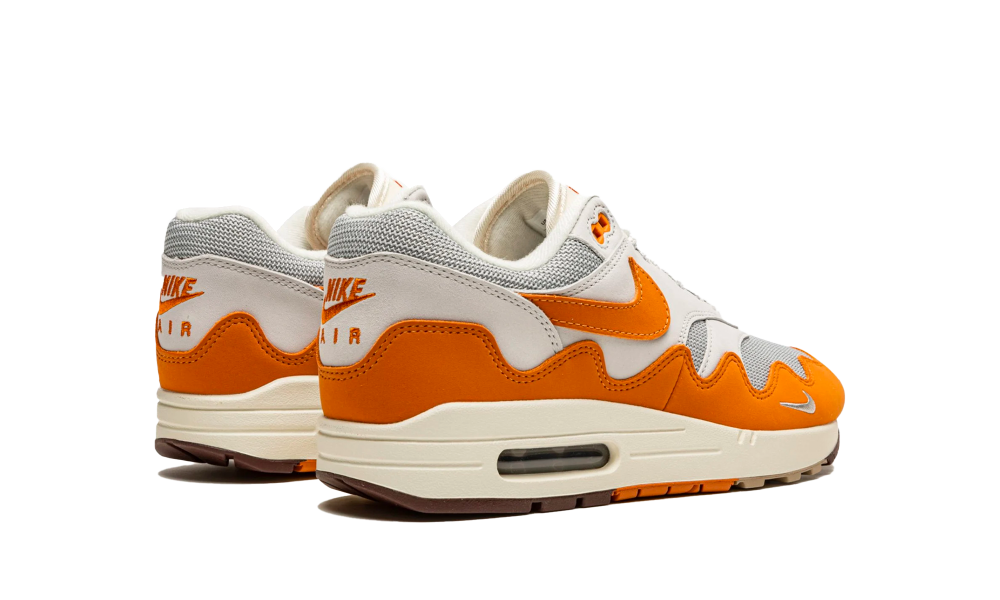 Pair of Nike Air Max 1 Patta Waves Monarch sneakers in white and orange with distinctive wave pattern, showcased from the back and side views, highlighting their exclusive design and cushioning technology.